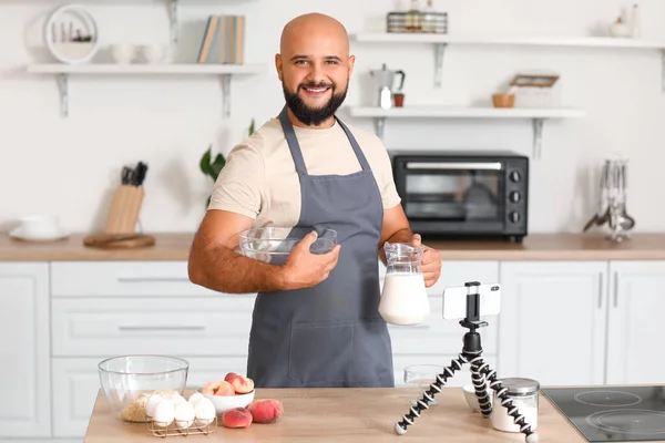 一个英俊的男人 从厨房的视频教学中获得了一壶牛奶和一碗烹调 — 图库照片
