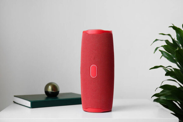 Wireless portable speaker on bedside table and houseplant near light wall, close seup
