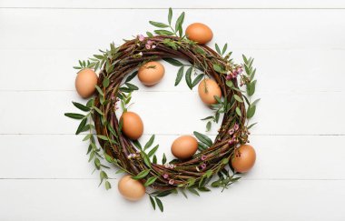 Beyaz ahşap arka planda yumurta, çiçek ve yapraklı Paskalya çelengi