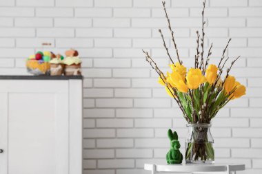 Vase with pussy willow branches and tulip flowers on table near white brick wall
