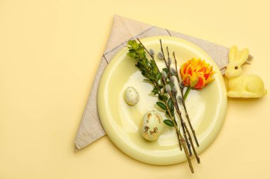 Plate with beautiful tulip flowers, pussy willow branches and painted Easter eggs on yellow background