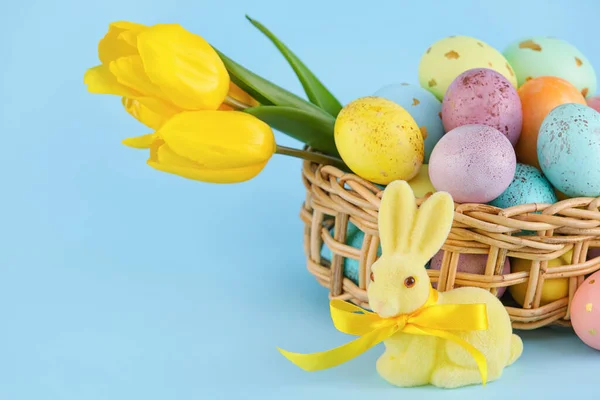 Rieten Mandje Met Geschilderde Paaseieren Bloemen Speelgoedkonijntje Blauwe Achtergrond — Stockfoto