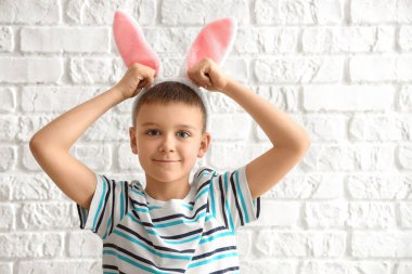 Beyaz tuğlalı arka planda tavşan kulaklı şirin bir çocuk.