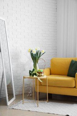 Rahat bir koltuk, çiçekli bir masa, Beyaz tuğla duvarın yanında paskalya dekoru.