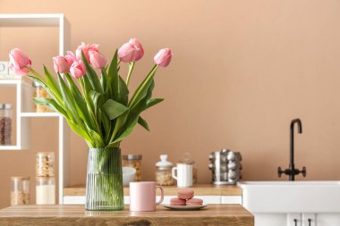 Mutfaktaki ahşap masada laleli vazo, fincan ve badem kurabiyesi.