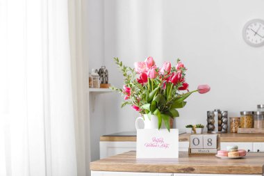 Çiçekli sürahi, badem kurabiyesi, küp takvimi ve açık mutfakta mutlu kadınlar günü yazılı tebrik kartı.