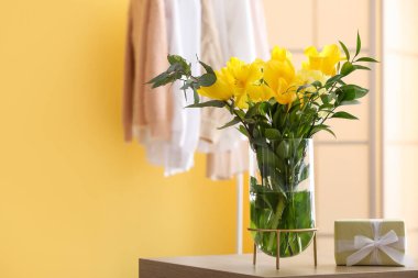 Sarı çiçekli vazo ve masadaki hediye.
