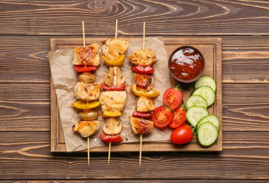 Ahşap arka planda sebzeli ızgara tavuk şişi ve sos.