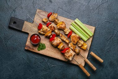 Ahşap tahta tahta tahta pano, sebzeli tavuk şişi ve siyah arka planda sos.