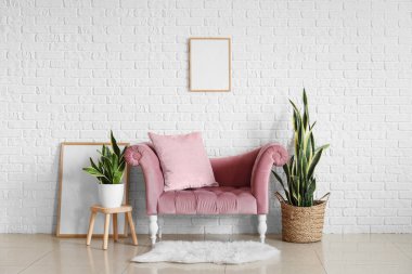 Beyaz tuğla duvarın yanında şık bir kanepe ve bitkiler.