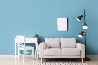 Şık bir kanepe, mavi duvarın yanında sandalye ve lamba var.