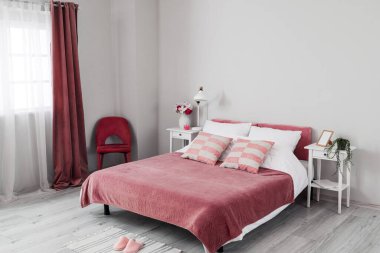 Rahat bir yatak, komodin ve ışık duvarının yanındaki sandalye.