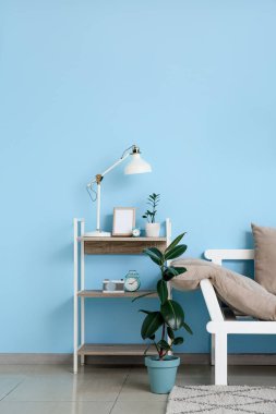 Rahat bir kanepe, çiçekler ve mavi duvarın yanındaki masada modern bir lamba.