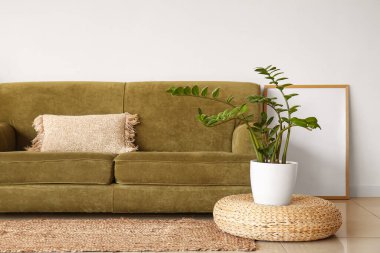 Rahat bir kanepe, çiçek ve beyaz duvarın yanında puf.