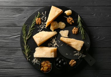 Siyah ahşap arka planda lezzetli parmesan peyniri parçaları olan tahta.