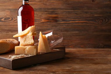 Ahşap arka planda lezzetli parmesan peyniri ve şarap kadehi parçaları olan tahta, yakın plan.