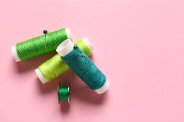 Pembe arka planda iplik makaraları ve top raptiyeleri