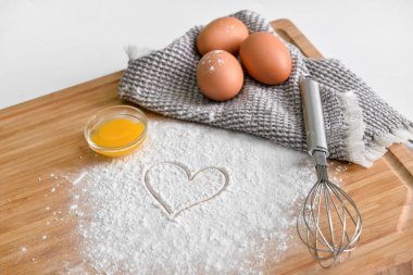 Tahta tahta tahta tahta, tavuk yumurtası, un, çizilmiş kalp ve hafif arka planda çırpma.