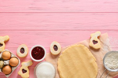 Paskalya kurabiyelerini pembe ahşap arka planda hazırlamak için hamur ve malzeme.