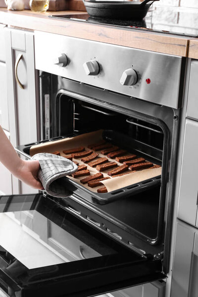 Женщина достает из духовки простыню с вкусными ржаными гренками