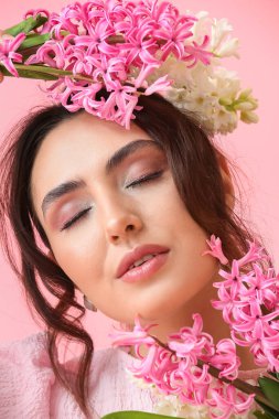 Pembe arka planda sümbül çiçekleri olan güzel genç bir kadın.