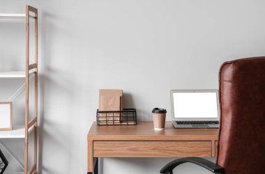 Ofis duvarının yanında dizüstü bilgisayarı ve kahve fincanı olan modern bir iş yeri.