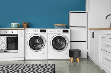 Modern çamaşır makineleri, fırın ve beyaz tezgahları olan şık bir mutfak.