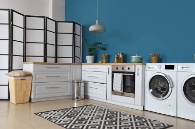 Modern çamaşır makineleri, fırın ve beyaz tezgahları olan şık bir mutfak.