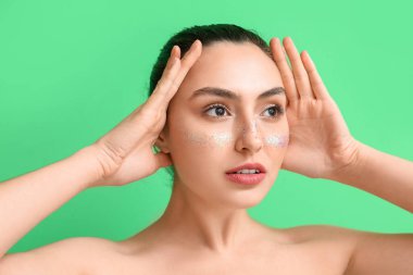 Yaratıcı makyajlı genç bir kadın yeşil arka plana bakıyor.