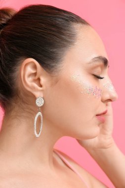 Gözleri kapalı ve pembe arka planda yaratıcı makyajı olan genç bir kadın.