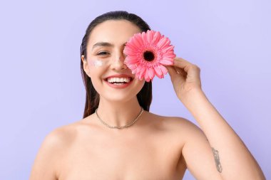 Yaratıcı makyajlı mutlu kadın yüzünü kapatıyor ve Gerbera çiçeğiyle renkleniyor.