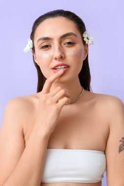 Yaratıcı makyajlı güzel bir kadın ve papatya çiçekleri renkli arka planda dudaklara dokunuyor.