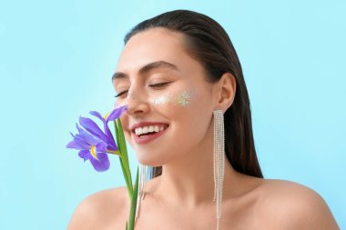 Mavi arka planda süsen çiçeği kokan yaratıcı makyajlı bir kadın.