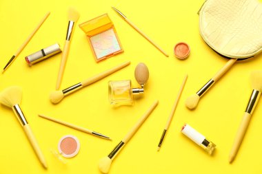 Sarı zemin üzerinde makyaj fırçaları ve kozmetik ürünleri olan kompozisyon
