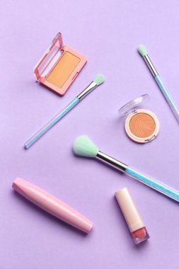 Mor zemin üzerinde makyaj fırçaları ve kozmetik ürünleri olan kompozisyon