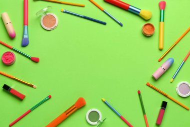 Yeşil zemin üzerinde makyaj fırçaları ve kozmetik ürünlerinden yapılmış çerçeve