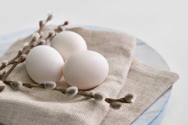 Wooden board with fresh chicken eggs and pussy willow branches on light background, closeup