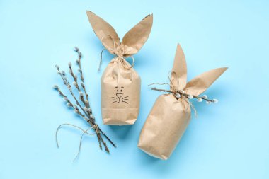 Easter bunny gift bags and pussy willow branches on color background
