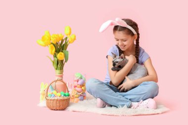 Sphynx kedisi olan küçük kız, Paskalya yumurtaları, pembe arka planda tavşanlar ve laleler.