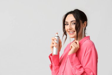 Gri arka planda saç spreyi olan güzel bir genç kadın.