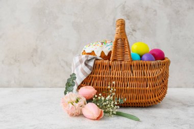 Renkli Paskalya yumurtaları, çiçekler ve açık arkaplanda pasta olan hediye sepeti.