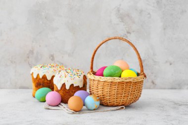 Açık arkaplanda boyanmış Paskalya yumurtaları ve kekleri olan hediye sepeti.