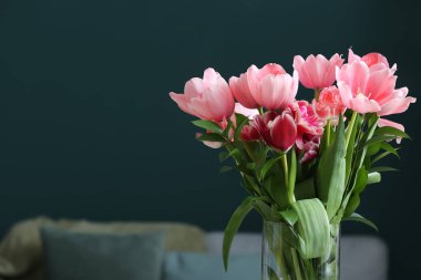 Karanlık oturma odasında pembe laleli cam vazo, yakın plan.