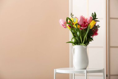 Masada bahar çiçekleri ve bej duvarın yanında katlanan bir vazo.