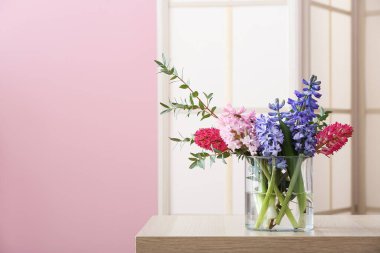 Masada bahar çiçekleri ve pembe duvarın yanında katlanan bir vazo.