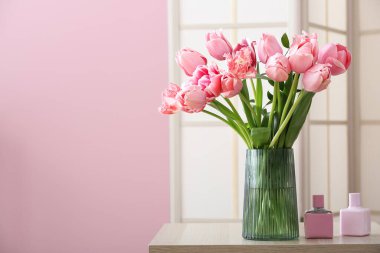 Odada pembe laleler ve parfüm şişeleri olan bir vazo.