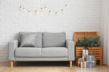 Çekmece dalları, Noel hediyeleri ve beyaz tuğla duvarın yanındaki kanepe.