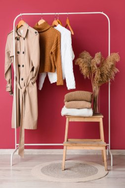Rafta, taburede kalın elbiseler ve pembe duvarın yanında vazo.