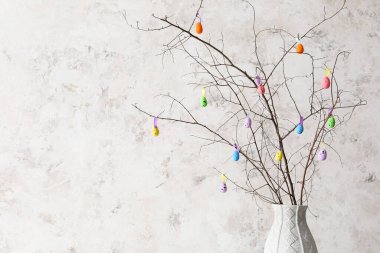 Ağaç dalları ve ışık duvarının yanında renkli Paskalya yumurtaları olan vazo.