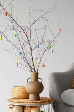 Ağaç dallı vazo, renkli Paskalya yumurtası ve sepeti ışık duvarının yanındaki masada.